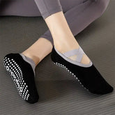 Black yoga socks with non-slip white rubber dot worn by a person on a grey surface